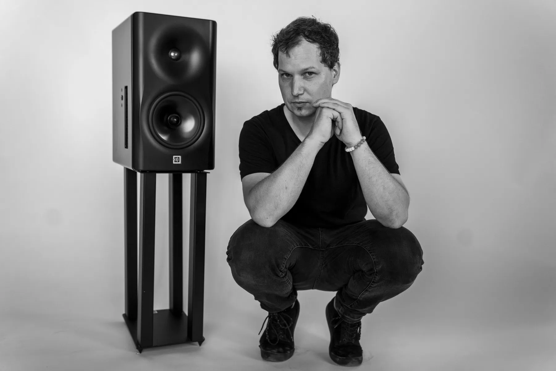 Márton Fenyvesi crouching beside a Dutch & Dutch 8c studio monitor, black and white.